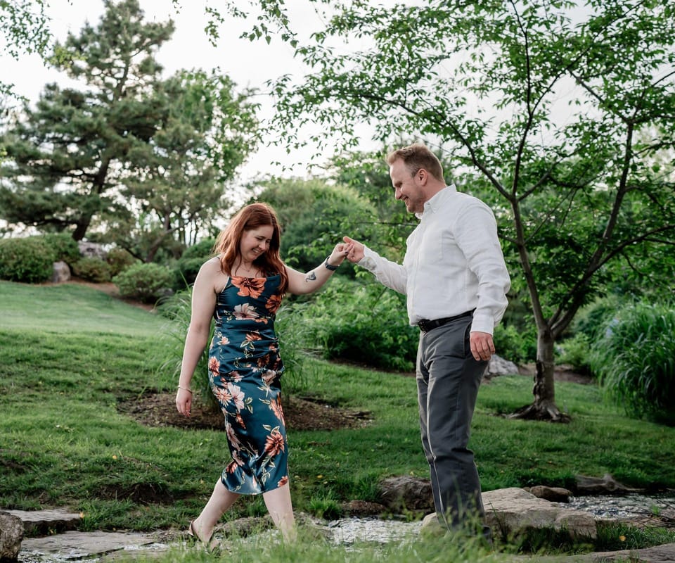 Steve holding Katie's hand as she steps across a small stream in a garden