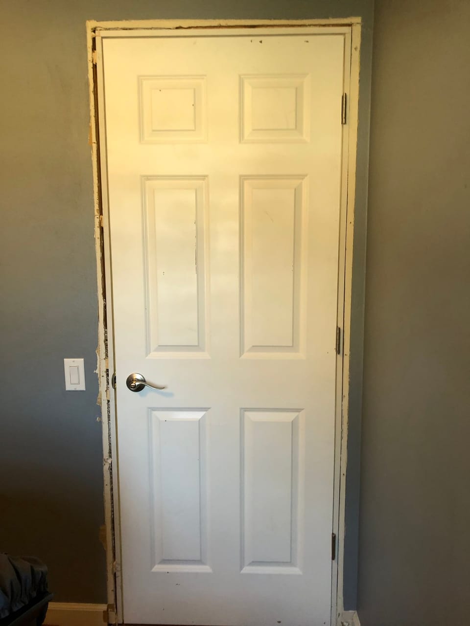 A white six-panel interior door hung in its new frame, the trim not yet on and the wall around it still rough