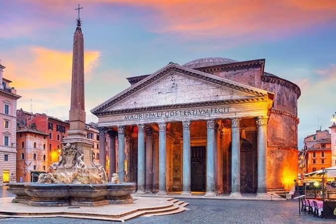The Pantheon in Rome at dusk, its columned portico lit gold beside the obelisk fountain of the Piazza della Rotonda
